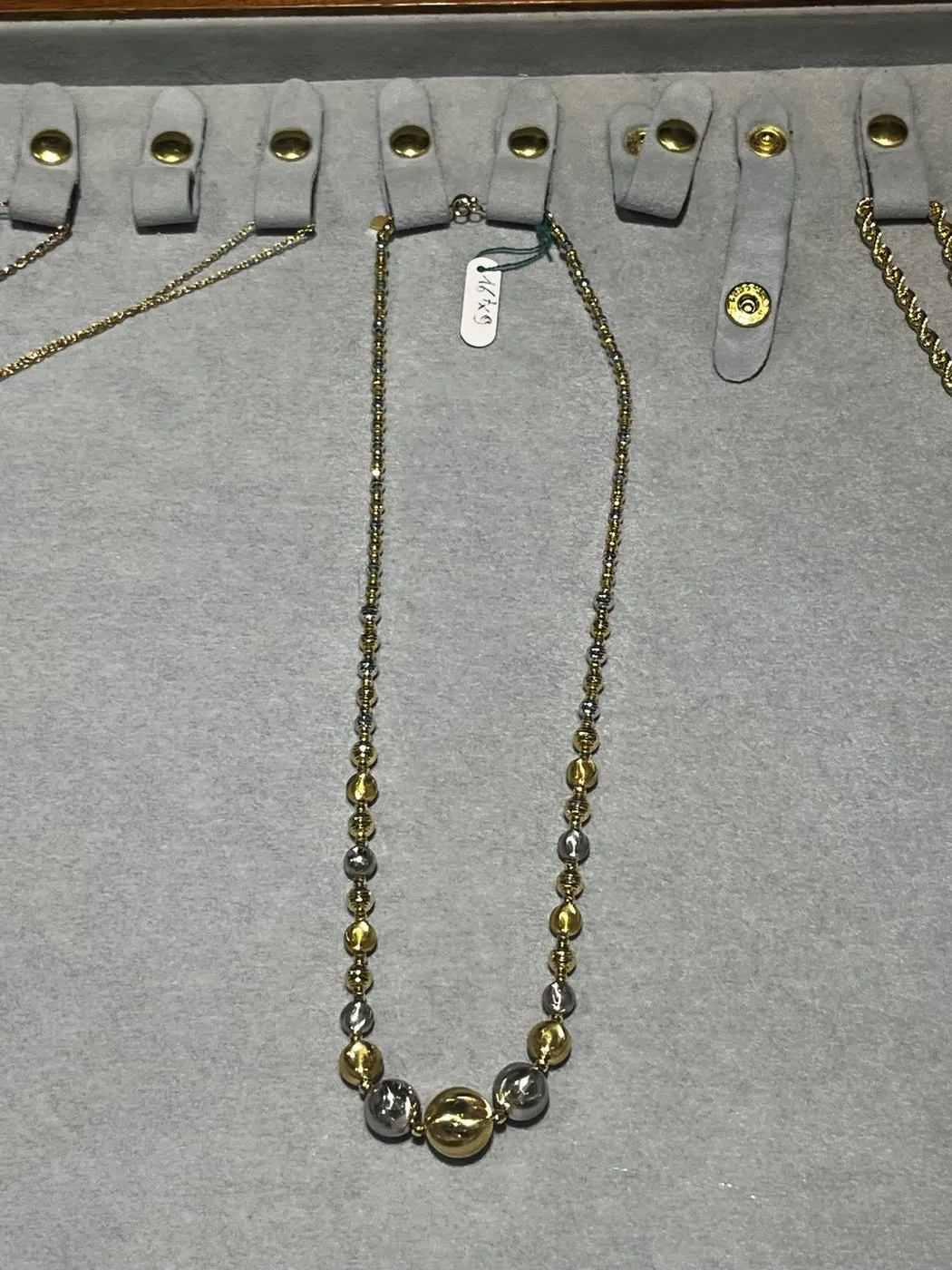 Fotografia reale scattata con il telefono della collana Vergottini a sfere oro e argento sul vassoio della boutique